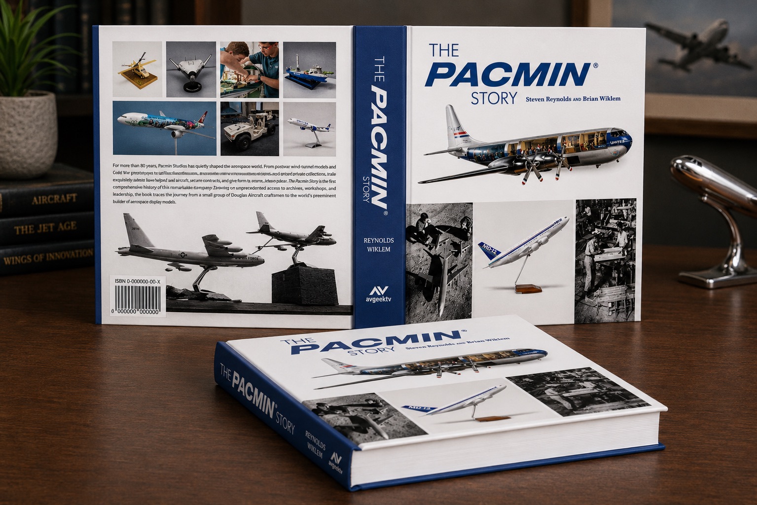 The Pacmin Story hardcover book displayed on a wooden desk, showing the front cover with a cutaway United Airlines propeller airplane model and the back cover featuring photographs of Pacmin's aerospace display models